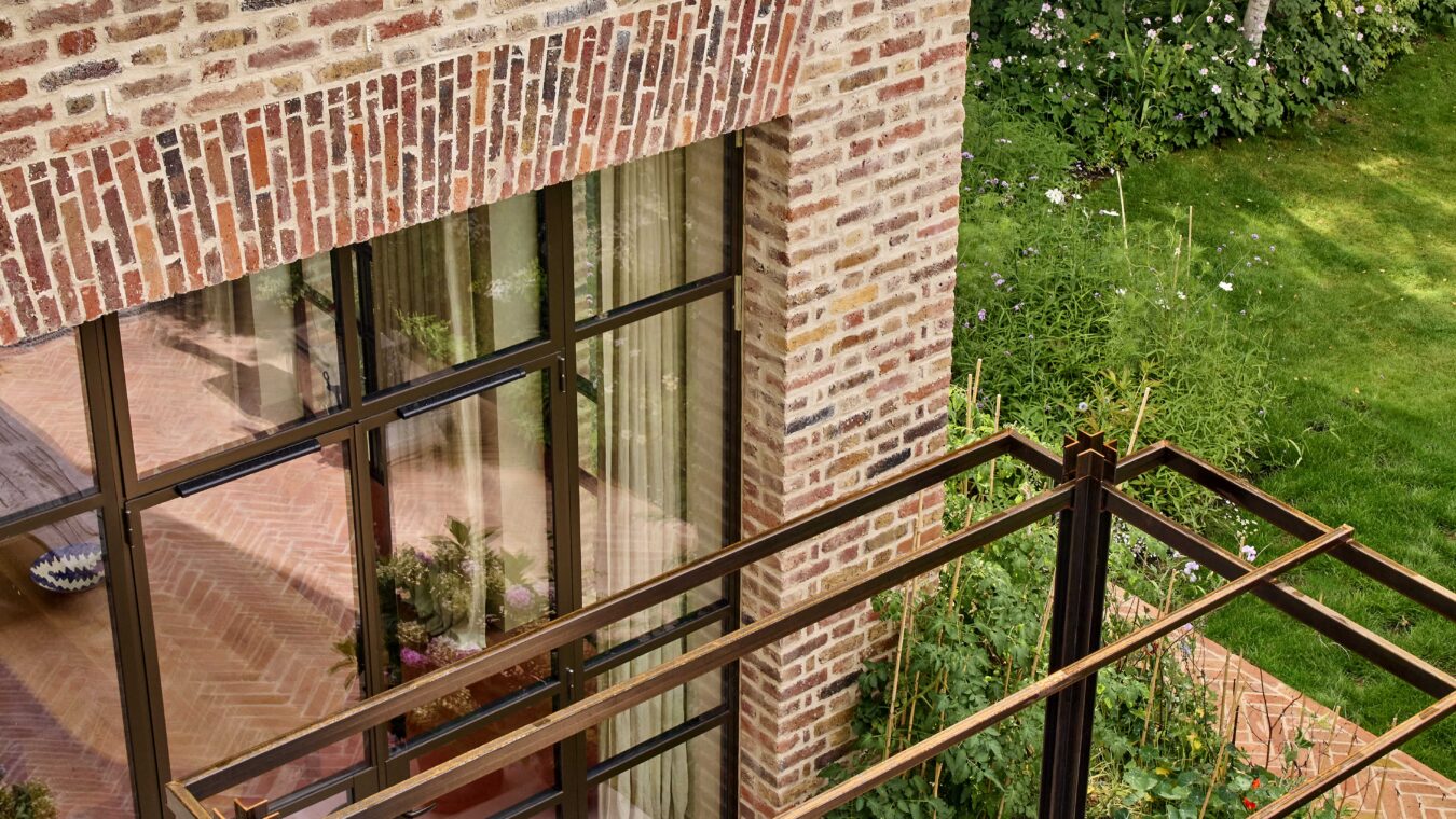 Close up detail of the brick facade and large modern window framed by the pergola