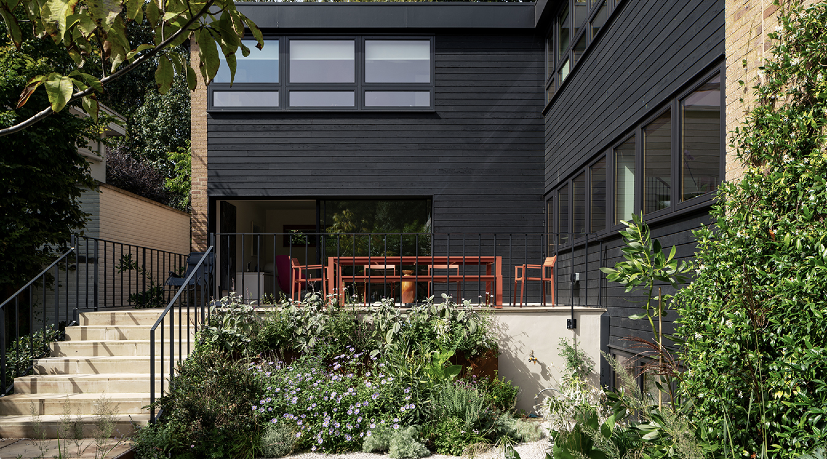 Exterior view of Mid-Century House featuring dark siding and tiered patio